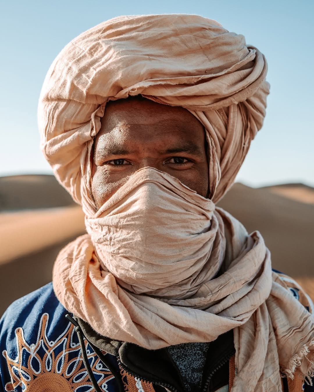 Abdo, desert cook and cultural host, looking into the camera with a pale scarf.
