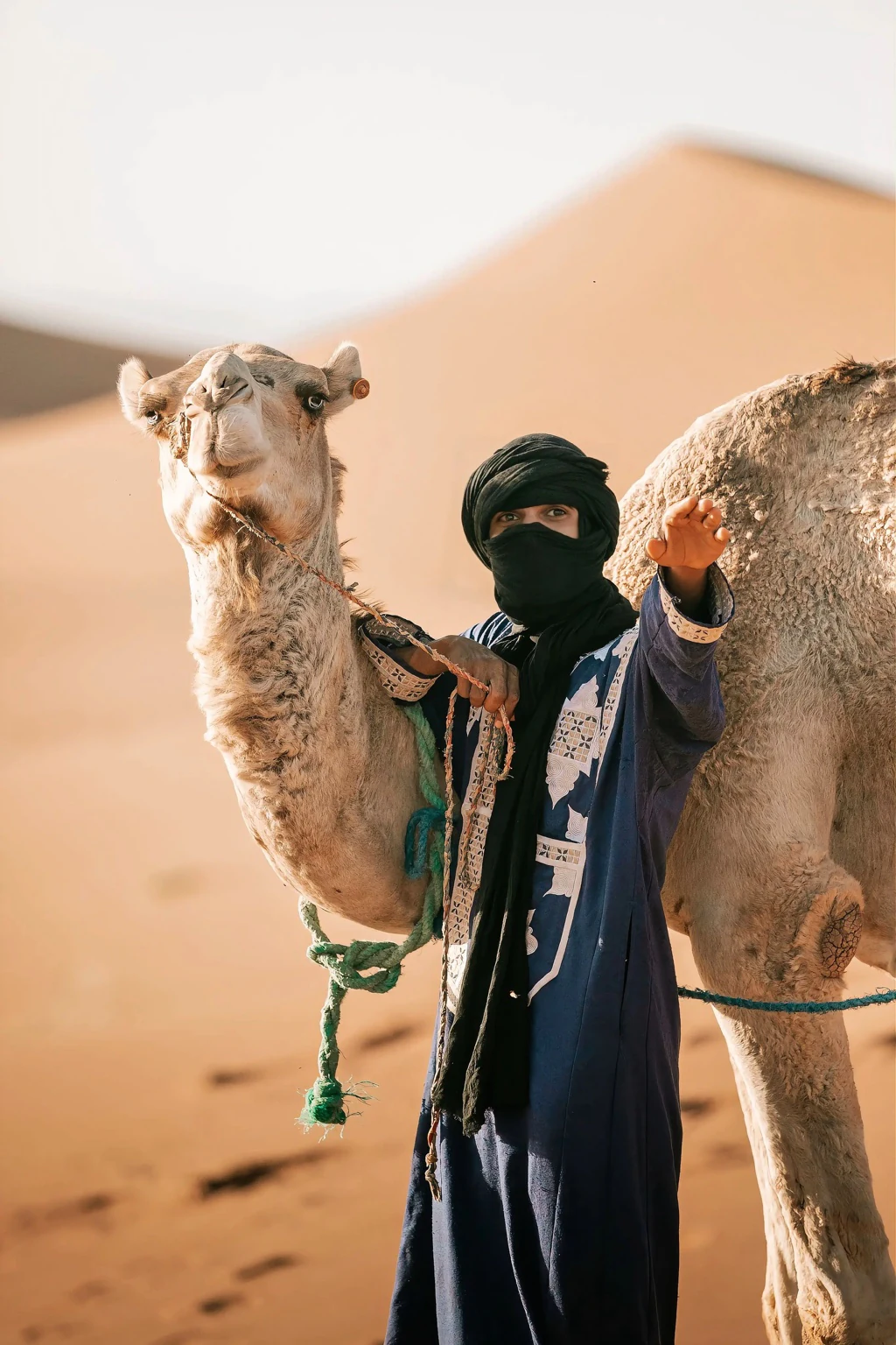 Ali El Gasmi, founder and nomad guide of Sahara Caravan, standing beside a camel in the dunes.