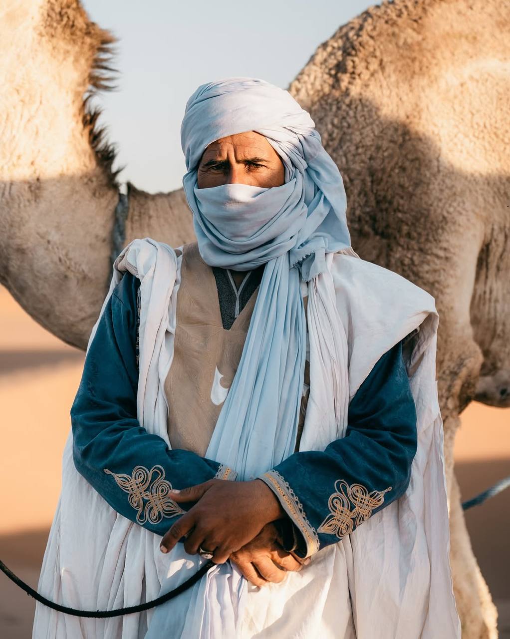 Hama, desert guide and cook of Sahara Caravan, standing in the Sahara with camels.