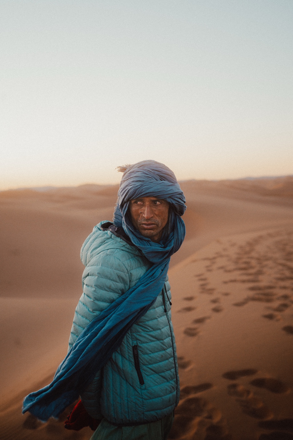 Hsayn, camel guide, standing among Sahara dunes in a blue robe.